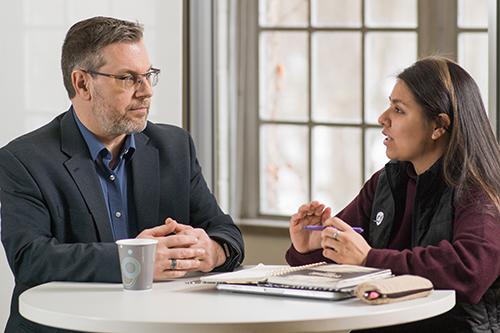 man and student talking at desk